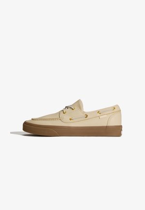 Beige læder bådsko med brun gummisål, guld øjenhuller, hvide snørebånd og mokkasinsyning.