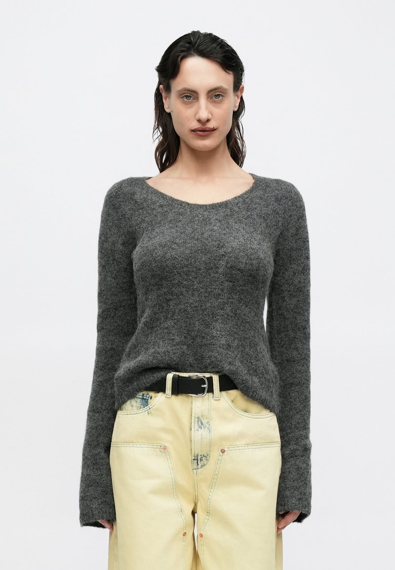 Pulover gri, tricotat, cu gât rotund și mâneci lungi, asortat cu pantaloni galben pal, cu buzunare mari în față și curea neagră.