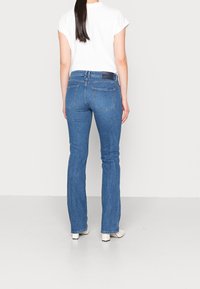Jeans de mezclilla azul acampanados con una cintura a media altura, que cuentan con bolsillos traseros y una sutil textura desgastada. Combinados con una camiseta blanca de manga corta.