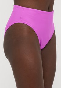 Μπικίνι σλιπ με ψηλή μέση σε φωτεινό ροζ, κατασκευασμένο από απαλό, ελαστικό υλικό. Διαθέτει καθαρό και απλό σχέδιο χωρίς επιπλέον διακοσμήσεις.