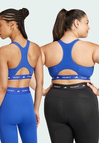 Blue athletic bras with cut-out back details, paired with blue and black high-waisted leggings featuring TECHFIT branding on the waistbands.