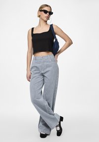 Fekete crop top, kék és fehér csíkos, bő szárú nadrág, fekete tömör sarkú cipők és egy kis kék farmer válltáska. Kerek napszemüveg.