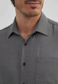 Chemise à manches courtes avec un motif texturé noir et blanc. Présente un devant à boutons, un col pointu et un détail de poche sur la poitrine.