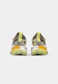 Chaussures de sport avec un schéma de couleurs marron, blanc et jaune ; matériaux synthétiques et textiles texturés ; talon rembourré avec une languette de traction.