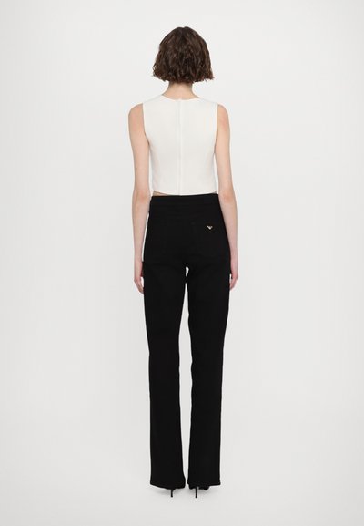 White sleeveless top with a back zipper, paired with high-waisted black trousers featuring a subtle logo on the back pocket.