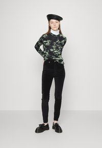 Calças de veludo cotelê pretas, blusa de mangas longas em mármore verde, gola alta branca por baixo, boina preta e sapatos pretos com um detalhe em laço.