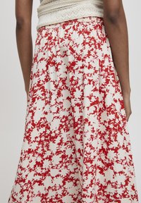 Gonna midi con fantasia floreale bianca e macchie rosse. Presenta una vita elasticizzata e un tessuto fluido per comfort e facilità di movimento.