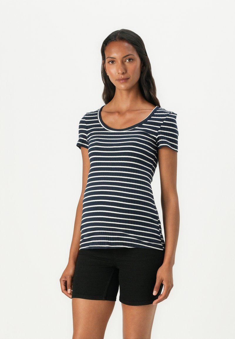 Μπλούζα με ρίγες ναυτικού σε κοντό μανίκι και στρογγυλή λαιμόκοψη, φτιαγμένη από ραμμένο ύφασμα. Συνδυασμένη με μαύρες βερμούδες, αναδεικνύει μια εφαρμοστή σιλουέτα.