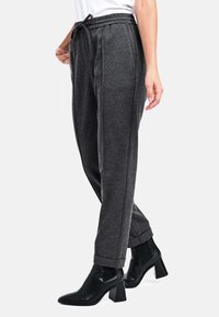 Graue, schmal zulaufende Jogginghosen mit einem Kordelzugbund und seitlichen Taschen, die eine weiche Textur und gerippte Bündchen aufweisen, kombiniert mit schwarzen Stiefeletten.