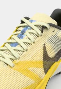 Nike teniske cipele s teksturiranim žutim i sivim gornjim dijelom, svijetlozelenim vezicama i sjajnom plavom oznakom. Crni detalji i izdržljiva potplat.