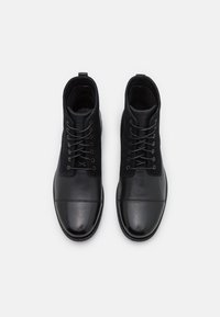 Paire de bottes à lacets en cuir noir et daim, vues de dessus, sur un fond gris clair uni.