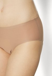 Neredzami, vidēja augstuma apakšveļa nude tonī. Veidota no gludas, elastīgas auduma ar minimālu apdari, lai nodrošinātu ērtu piegulšanu.
