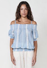 Blusa azzurro chiaro fuori spalla con maniche a sbuffo, caratterizzata da motivi ricamati bianchi e una finitura testurizzata. Tessuto morbido e vestibilità comoda.