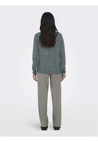 Un pull gris à côtes avec des manches longues et un ourlet arrondi, associé à un pantalon large gris clair et des chaussures noires.