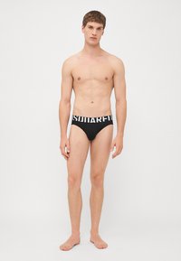 Black brief-style underwear with a wide waistband featuring bold white lettering. Made from smooth fabric, showcasing a fitted design.