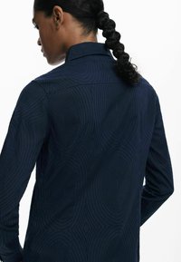 Marineblaue Langarmbluse mit einem strukturierten Muster aus konzentrischen Kreisen und Rauten, klassischem Kragen und knöpfbarem Stil.