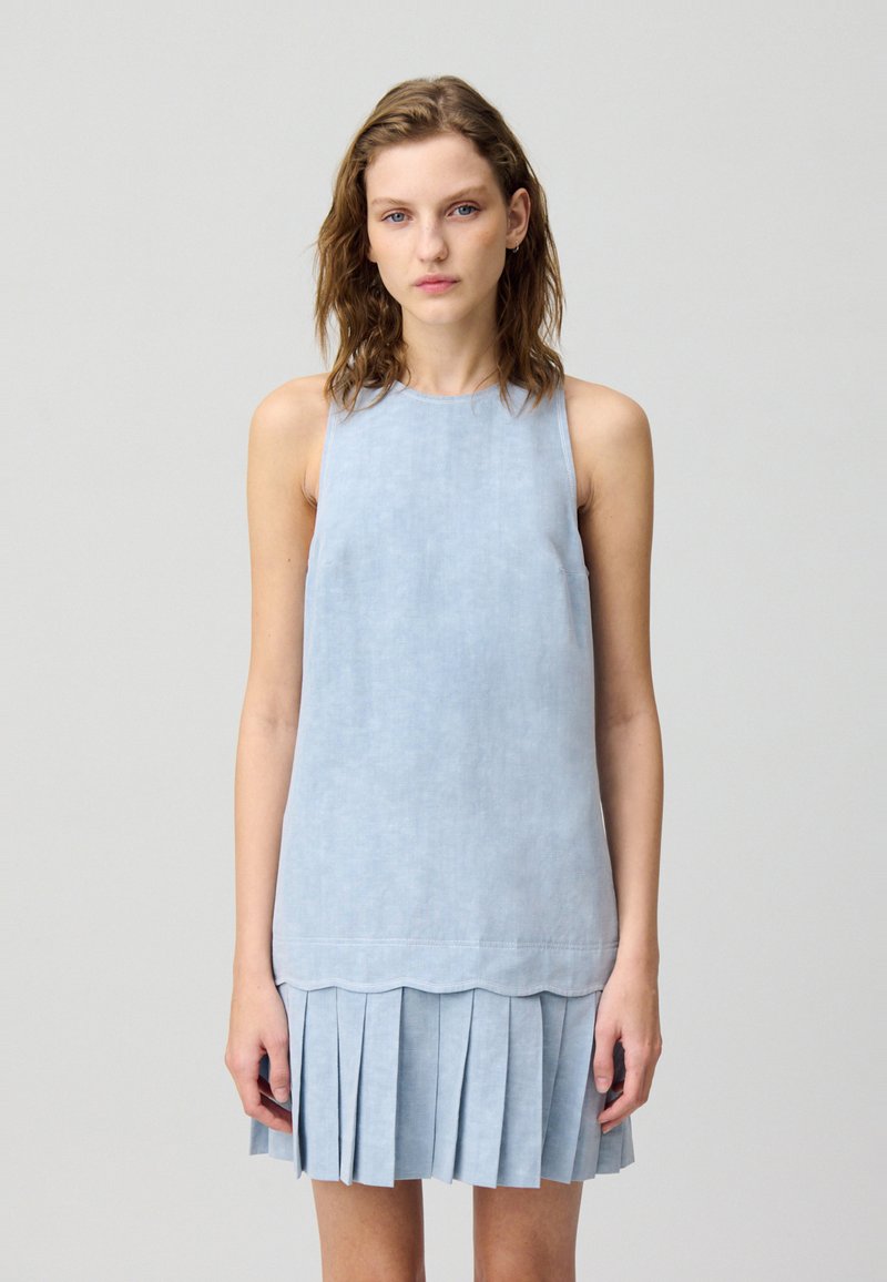 Robe sans manches bleu clair en tissu texturé avec une coupe droite et une jupe plissée. Présente un ourlet festonné à la taille.