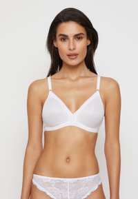 Bralette blanc côtelé avec un décolleté en V profond et des bretelles fines, comportant des éléments en métal argenté. Le design inclut une texture lisse et des accents subtils.