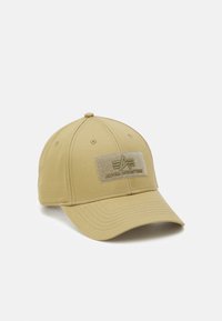 Beige baseballkeps i tyg med en frontficka märkt "ALPHA INDUSTRIE", krökt skärm och sex ventilationshål.