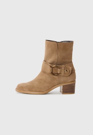 Stivale alla caviglia in suede beige con punta rotonda, una larga fascia con una fibbia circolare e un tacco in legno impilato. Texture liscia.