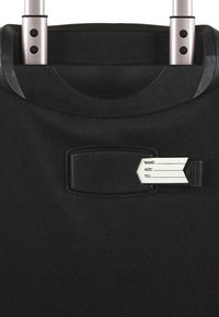 Maleta de tela negra con asa extensible, que cuenta con un portatarjetas para nombre con una etiqueta blanca para información personal. Superficie suave y con textura.