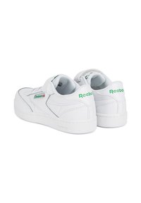 Białe skórzane sneakersy z grubą podeszwą, rzepem oraz zielonym logo Reebok. Perforowane detale po bokach dodają faktury.