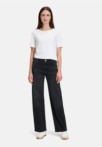 Szerokie czarne dżinsy z wysokim stanem, zestawione z gładką białą koszulką. Model nosi białe trampki i stoi na jednolitym tle.