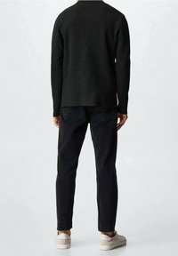 Maglione nero lavorato a maglia con scollatura rotonda, indossato sopra jeans scuri, completato con scarpe casual di colore chiaro. Stile semplice e vestibilità rilassata.