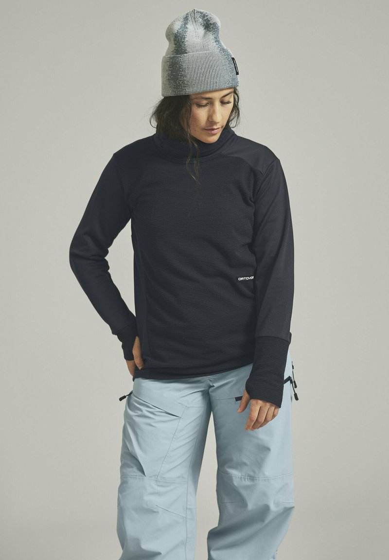 Schwarzes Thermoshirt mit langen Ärmeln und hohem Kragen; hellblaue Schneehose mit Taschen und Reißverschlüssen; strukturierte graue Mütze.