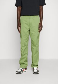 Groene cargo pants met een comfortabele pasvorm, elastische tailleband en zijzakken, gecombineerd met zwart-witte sneakers.