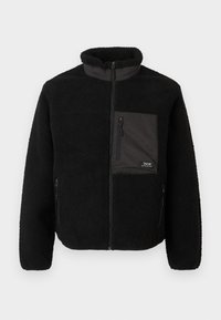 Giacca in pile nera con colletto alto, chiusura con zip e una tasca sul petto. Presenta un tessuto texturizzato e due tasche laterali con zip.