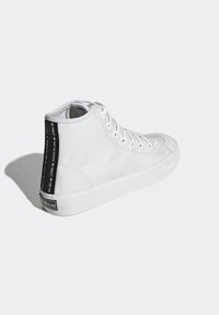 White high-top sneaker made of canvas, featuring a rubber sole, side logo detailing, and lace-up closure with metal eyelets.