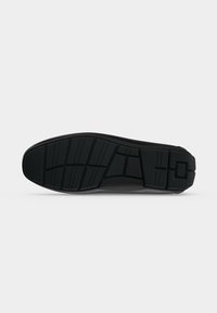Semelle de chaussure noire avec motifs géométriques de la bande de roulement sur un fond neutre uni, montrant la vue inférieure d'une chaussure habillée.