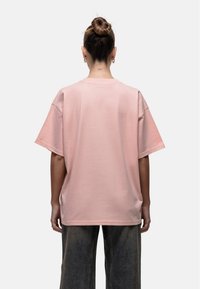 Różowa, oversize'owa koszulka z gładkiego bawełnianego materiału, z krótkimi rękawami, okrągłym dekoltem i luźnym krojem. Widok z tyłu.