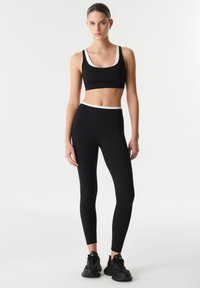 Black athletic set featuring a cropped top with white accents and high-waisted leggings. Smooth fabric, form-fitting design, and minimalist style.