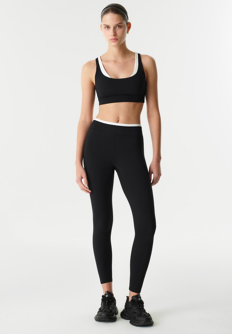 Completo sportivo nero composto da top cropped con accenti bianchi e leggings a vita alta. Tessuto liscio, design aderente e stile minimalista.