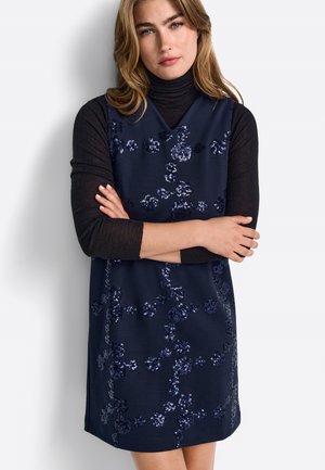 Marineblaues ärmelloses Kleid mit V-Ausschnitt, verziert mit floralen Paillettenmustern, kombiniert mit einem schwarzen Rollkragenpullover. Glatte Textur, über knielang.