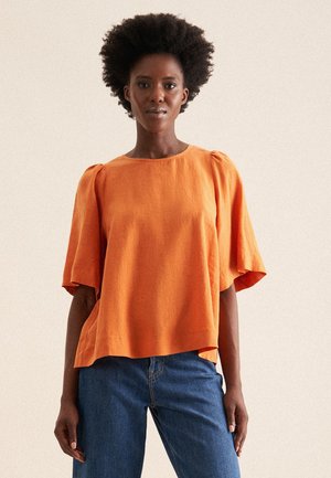 Top in lino arancione a vestibilità ampia con maniche corte a campana e scollatura rotonda, abbinato a jeans in denim blu. Tessuto testurizzato.