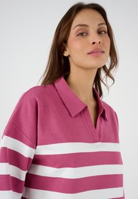 Pullover a righe rosa e bianche con colletto. Il tessuto ha una texture liscia, presenta ampie righe orizzontali ed ha un fit rilassato.