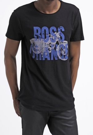 Uomo che indossa una maglietta nera con scritta blu sbiadita "BOSS ORANGE" e grafica di una moto sul davanti.