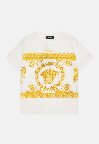 Biała koszulka z krótkim rękawem, zdobiona złotymi, bogatymi wzorami barokowymi oraz emblematem głowy Meduzy otoczonej wieńcem laurowym, nad wzorem logo Versace.
