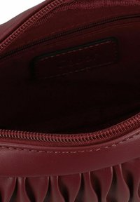 Bordeauxfarbene, strukturierte Handtasche mit Reißverschluss. Das Innere verfügt über ein glattes Futter und ein kleines Etikett. Gathered-Details am Öffnung.