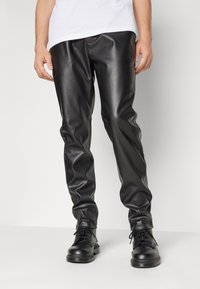 Schwarze Lederhosen mit einem eleganten Design, das eine glatte Textur und einen schlanken Schnitt aufweist. Kombiniert mit schwarzen Schnürstiefeln.