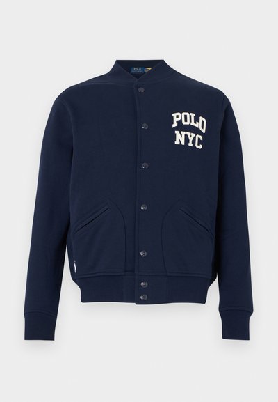 Μπλε ναυτικού κουμπωτό varsity μπουφάν με ριμπ μανσέτες και τελείωμα, μπροστινές τσέπες και λευκό κείμενο «POLO NYC» στο στήθος.