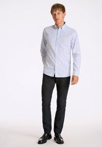 Lichtblauw overhemd met dunne witte strepen, lange mouwen en een scherpe kraag, gecombineerd met zwarte broek en glanzende zwarte schoenen.