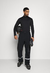 Tenue de sports d'hiver noire comprenant un haut à manches longues, un pantalon avec des accents réfléchissants, des gants et un casque. Bottes de couleur foncée avec des éléments en métal.