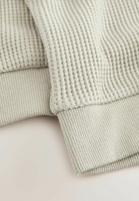 Tessuto grigio chiaro testurizzato con un design a coste e un bordo a manica liscio, che mostra un delicato e sottile motivo a intreccio.