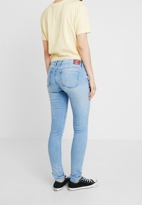Světlemodré slim džíny s vysokým pasem, pěticípým designem a jemnými švy, v kombinaci se žlutým tričkem a černými teniskami.