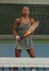Um jogador de ténis com um vestido atlético verde clarinho, segurando uma raquete de ténis laranja, com um fundo texturizado de um court e rede de limites.