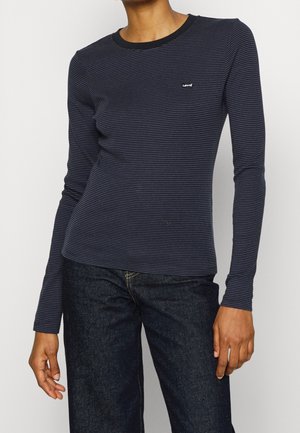 Personne portant un t-shirt ajusté à manches longues rayé bleu marine et noir avec le logo Levi’s et un jean bleu foncé.